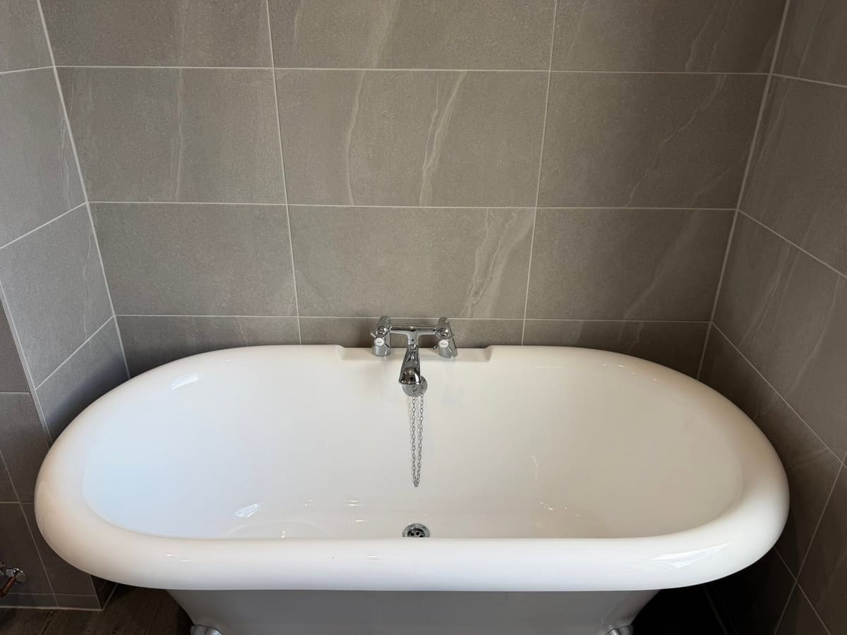 A roll-top bath with chrome taps, fitted by Graham against grey tiles