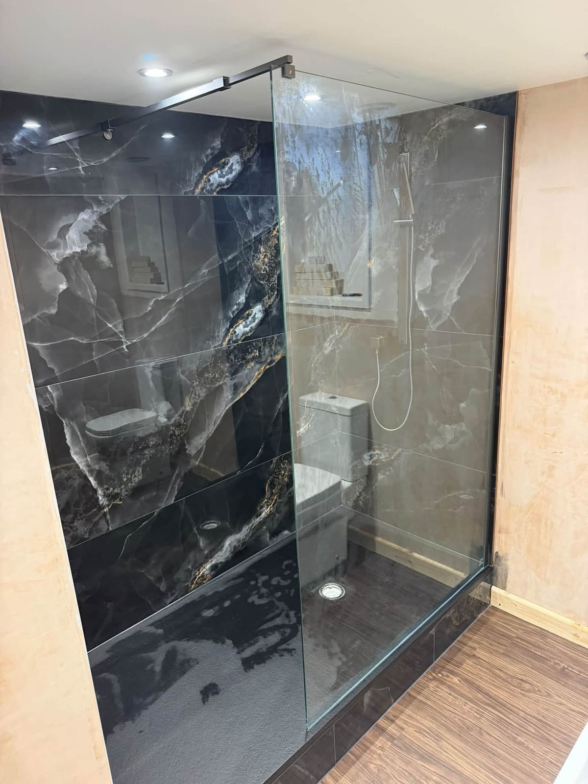 A complete bathroom installation in Rishworth, finished with dark marble-effect wall panels and a glass shower screen